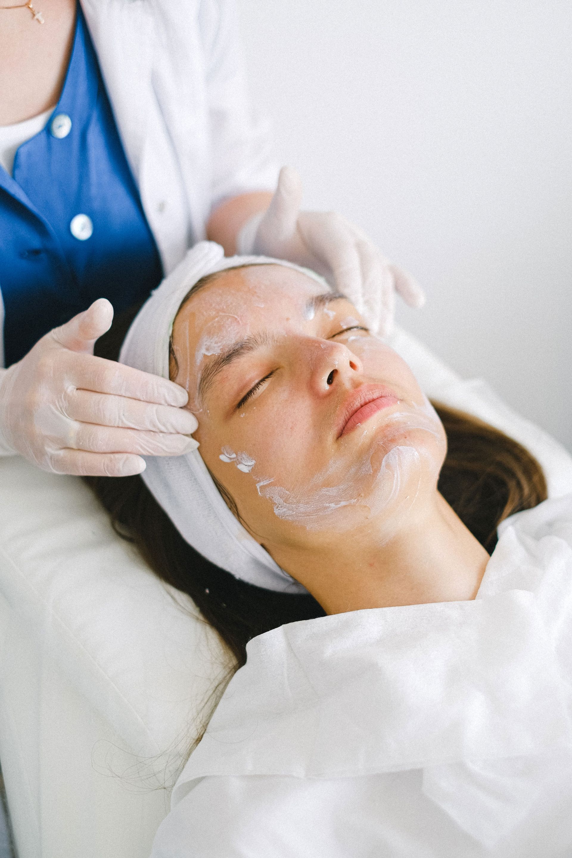From above of crop anonymous professional cosmetician massaging female client face with lotion during beauty session
